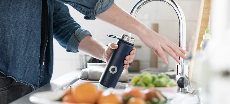 a person filling a grey bottle with water