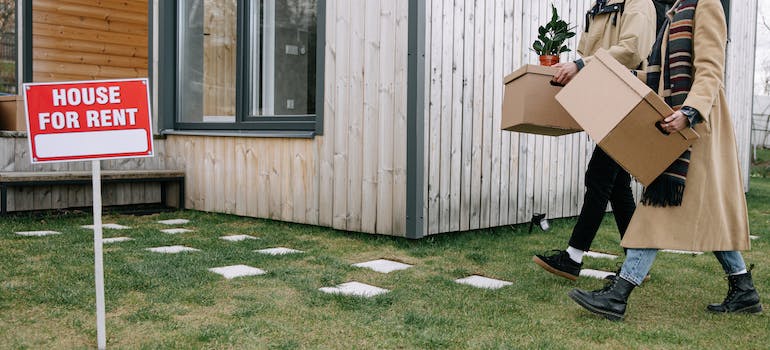 two people carrying cardboard boxes into a house for rent