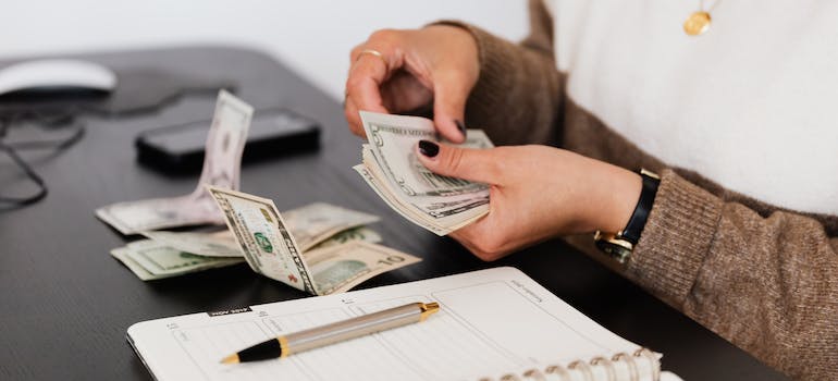 a woman with black nails counting dollar bills next to a notebook