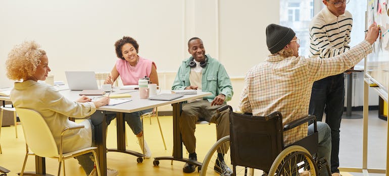 a man in a wheelchair writing something on a whiteboard during a meeting