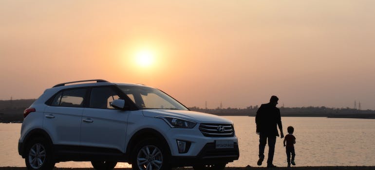 a man and a child in front of a white car at sunset