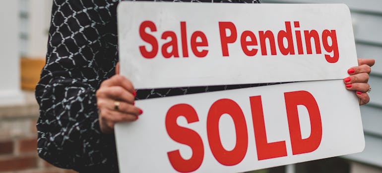 a woman holding two signs that indicate a sale was pending and then that it was sold