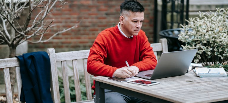 a man in a red sweater is researching something on his laptop