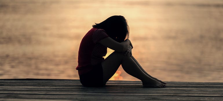 a woman feeling very sad while sitting next to the ocean