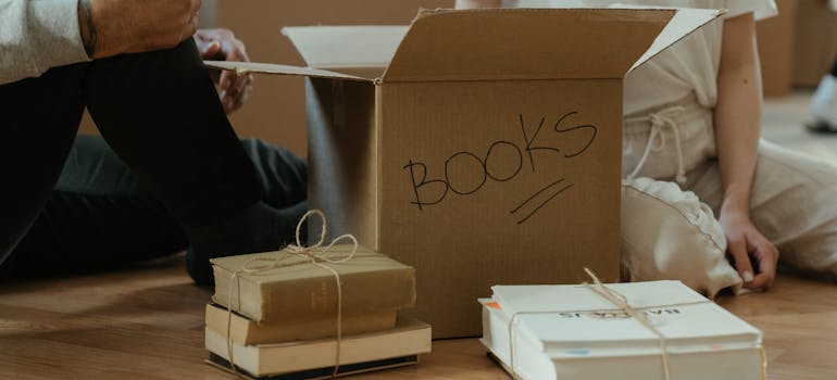 two people next to a box and several piles of books