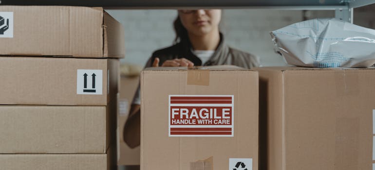 a woman putting a box on a shelf that obviously contains fragile items, which illustrates one of the reasons why you should hire professionals for your office move