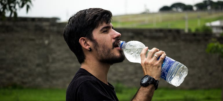 a man in a black shirt drinking water from a bottle to keep cool when it's too hot outside