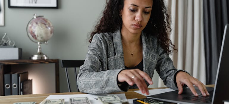 a woman with a serious look on her face is counting money and doing some calculations on a computer