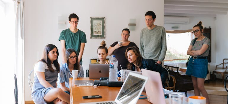 a group of young people looking at something on a laptop in an office