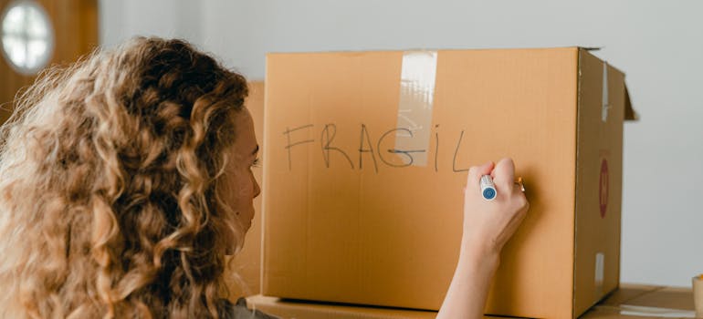 a woman writing the word "fragile" on a box with her belongings after learning about the common moving day myths