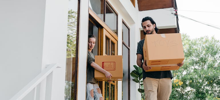 two people carrying cardboard boxes out of the house and down the stairs