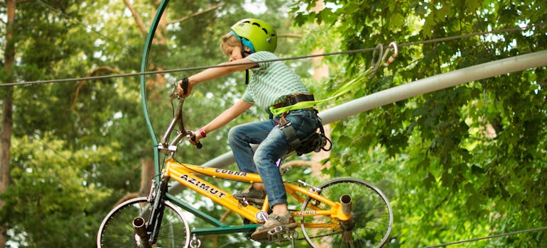 a boy riding a bike along a wire in an adventure park