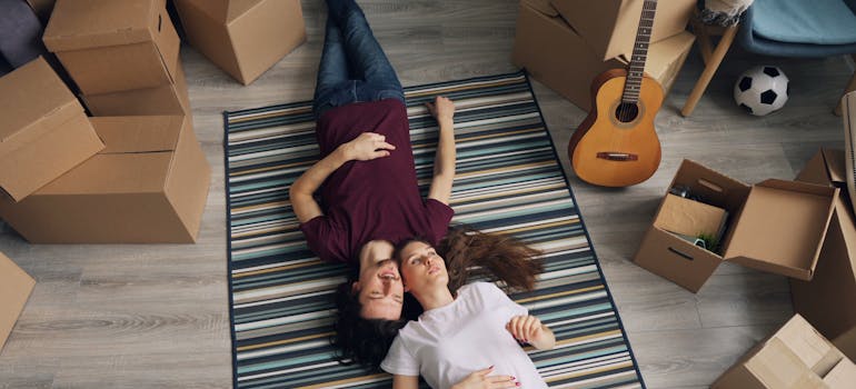 two people lying on the floor while surrounded by lots of different stuff and many cardboard boxes