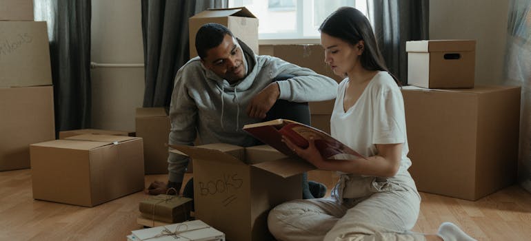 two people sitting on the floor next to some cardboard boxes and reading a scrapbook together