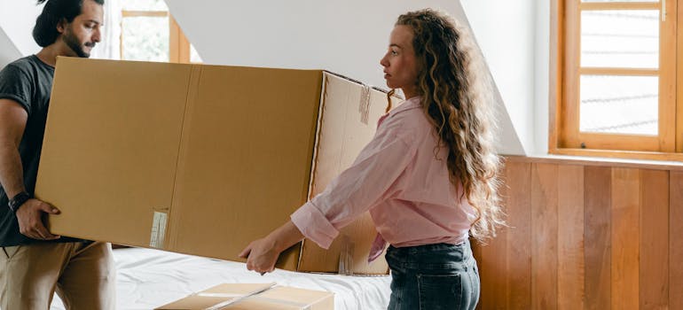 two people carrying a very large box through a bedroom