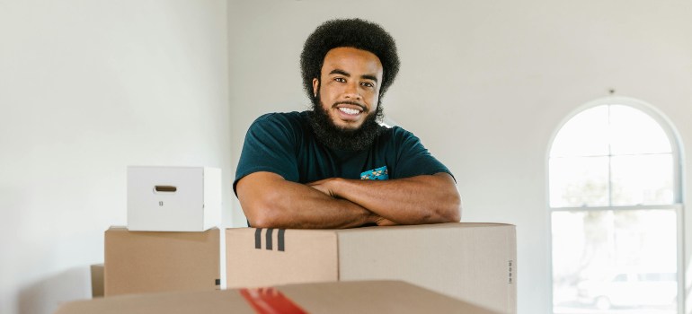 a man working as a professional mover is leaning on a cardboard box and smiling