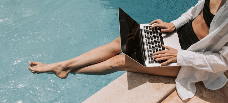 a woman researching pool cleaning mistakes to avoid while sitting next to her pool and holding a laptop