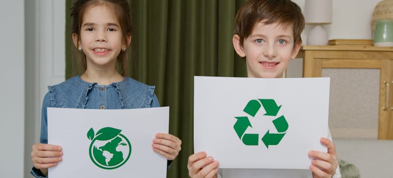 two kids holding drawings with the symbol of recycling, in reference to one of the Orange County laws new residents must know about