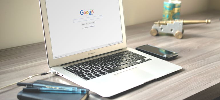 a laptop with a search engine on its screen and a phone and a pen next to it