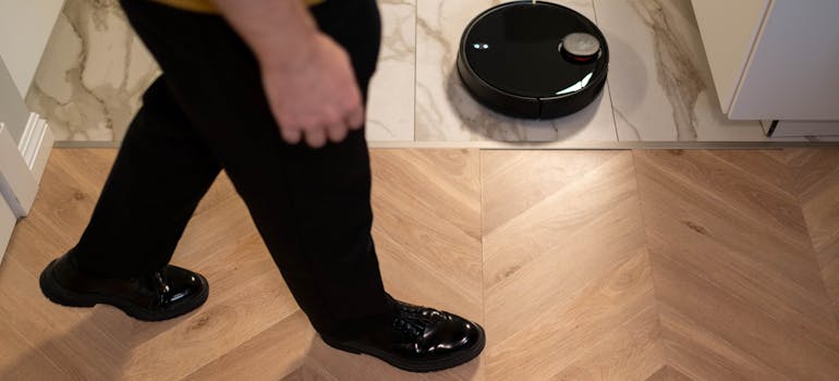 a man walking over the floor being cleaned by a robot vacuum cleaner