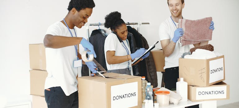 three people sorting their stuff into various boxes, most of which are for donation, because they need to move from one rental apartment to another