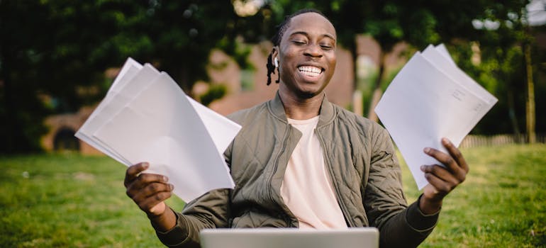 a man happily holding a bunch of papers while working on a laptop