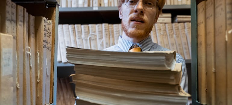 an office worker holding a pile of documents while standing in a company archive