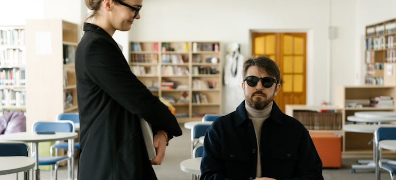 a blind man with glasses and a girl with a smile standing next to him in a school library