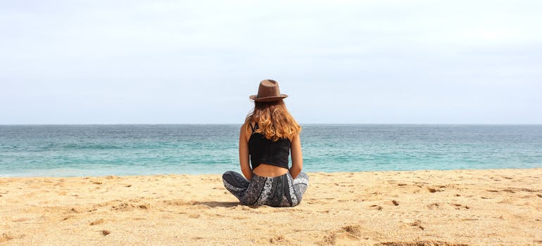 a woman with a hat is sitting on a beach