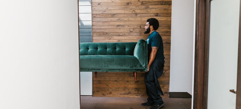 a professional mover carrying a velvet sofa out of a very modern house