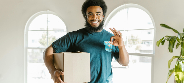 Smiling man holding a box and giving an 'okay' hand gesture.