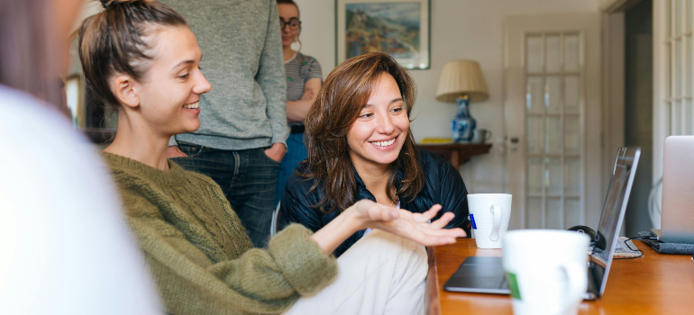 Friends gathered around a laptop, sharing ideas. A way to build a new routine after moving by connecting.