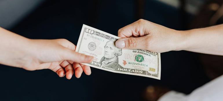 Person handing a $10 bill to another person, representing tipping practices for movers in Orange County.