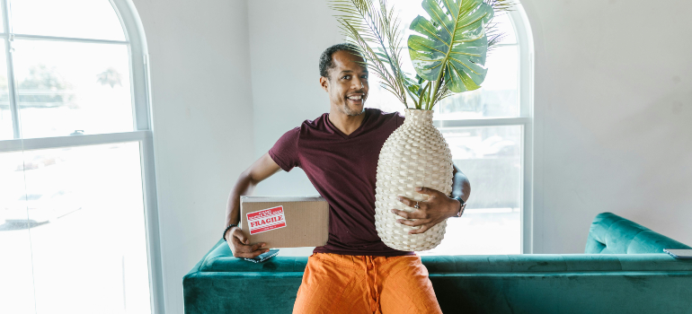 A mover holding a moving box and a vase. 