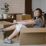 a woman sitting in a cardboard box before moving from Santa Ana to Irving