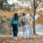 two people holding hands in the park where there are a lot of yellow trees