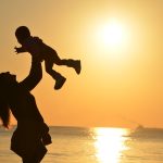 a woman holding a child in her arms at sunset near the beach