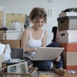 a woman working on her computer while surrounded by multiple boxes