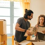 a couple packing their stuff into cardboard boxes and considering the benefits of moving to Garden Grove