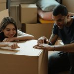 two people leaning onto a cardboard box and talking about the common things people forget to do when moving