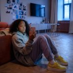 a teenager sitting on the floor with earphones and a smartphone in her hand