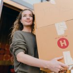 a woman carrying large cardboard boxes with a smile on her face