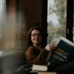 a woman smiling while reading newspapers in peace, after discovering one of the things you'll love about living alone