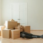 a man covered with a pile of cardboard boxes while lying on the floor